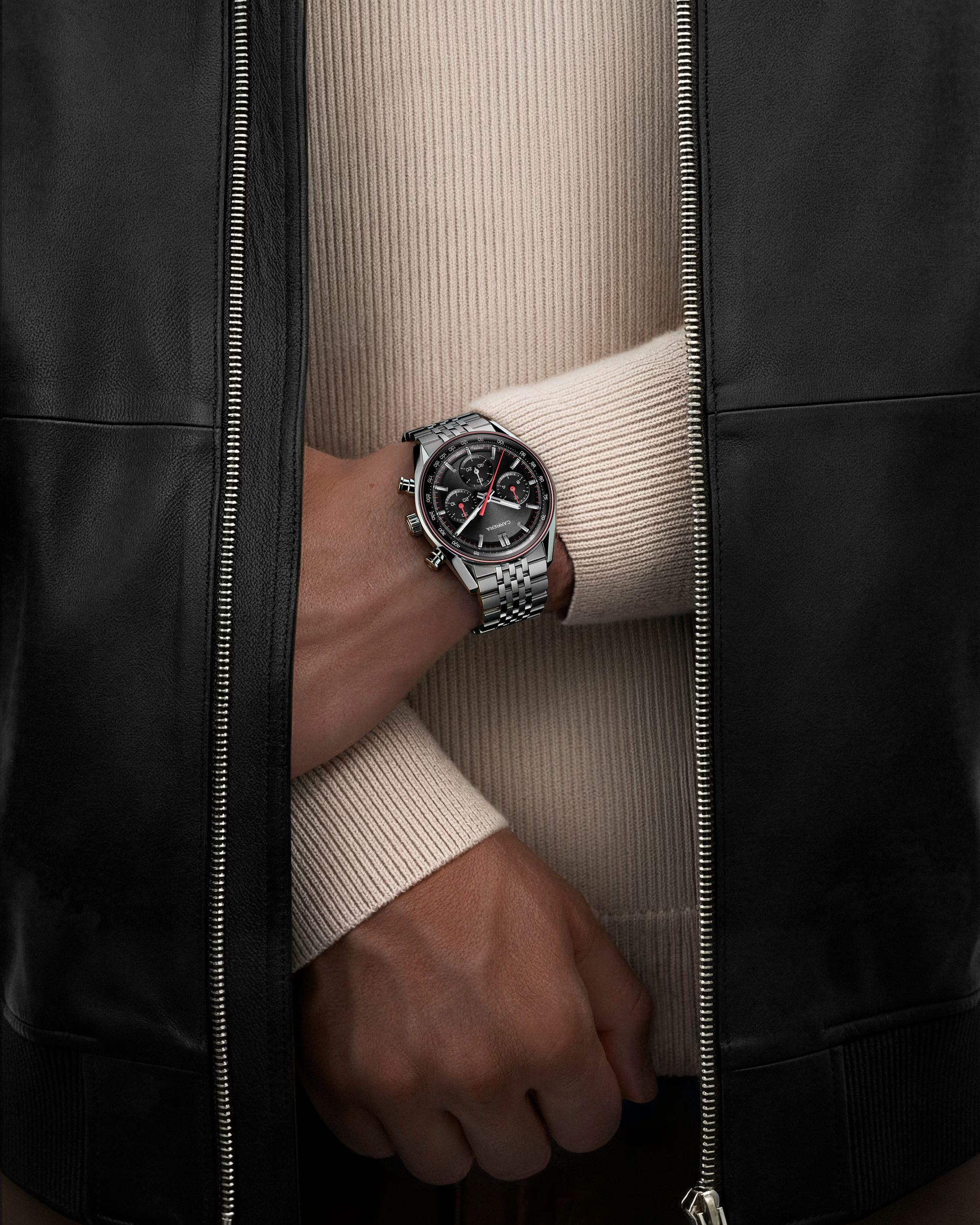 Person wearing a black leather jacket with a watch on a beige sweater